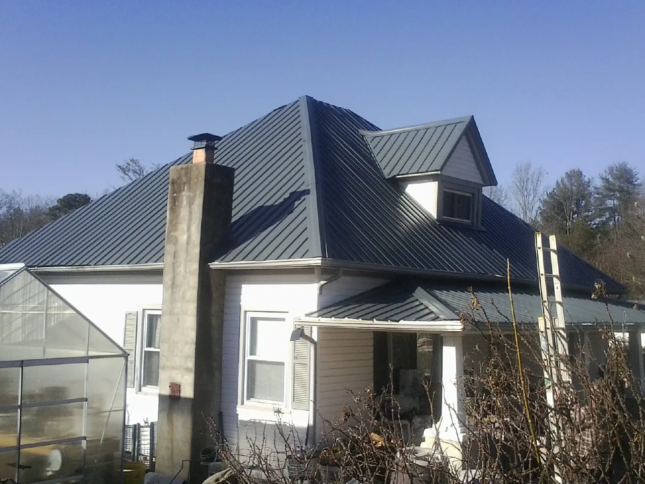 Dark blue standing seam metal roof on a white farmhouse with dormer — Slate & Tile Roof Repair by Roofing Brothers in East New Market