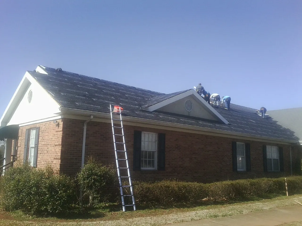 Crew tearing shingles off a brick ranch roof with a ladder set — Metal Roof Repair work by our crew in East New Market