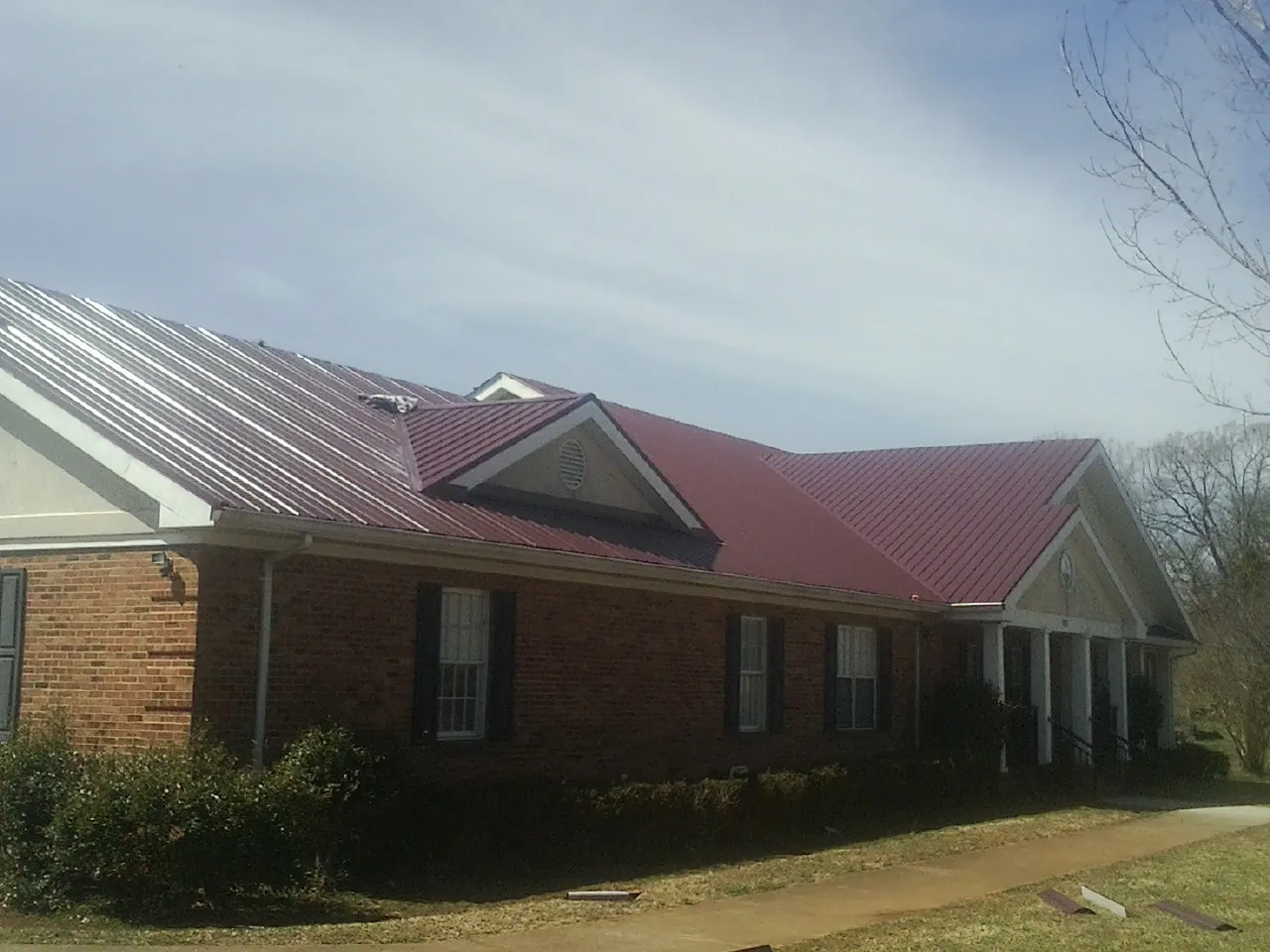 Red metal roof with gabled entries on a long brick building, from a Hail Damage Roof Repair job in East New Market
