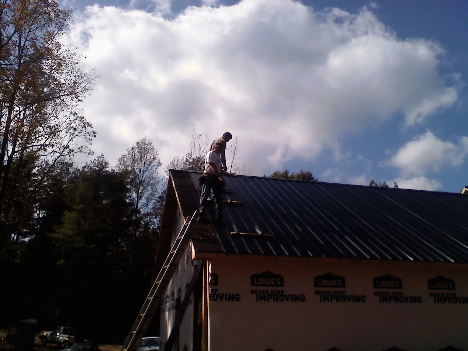 Roofer fastening dark metal panels high against a cloudy sky, from a Roof Inspection job in East New Market