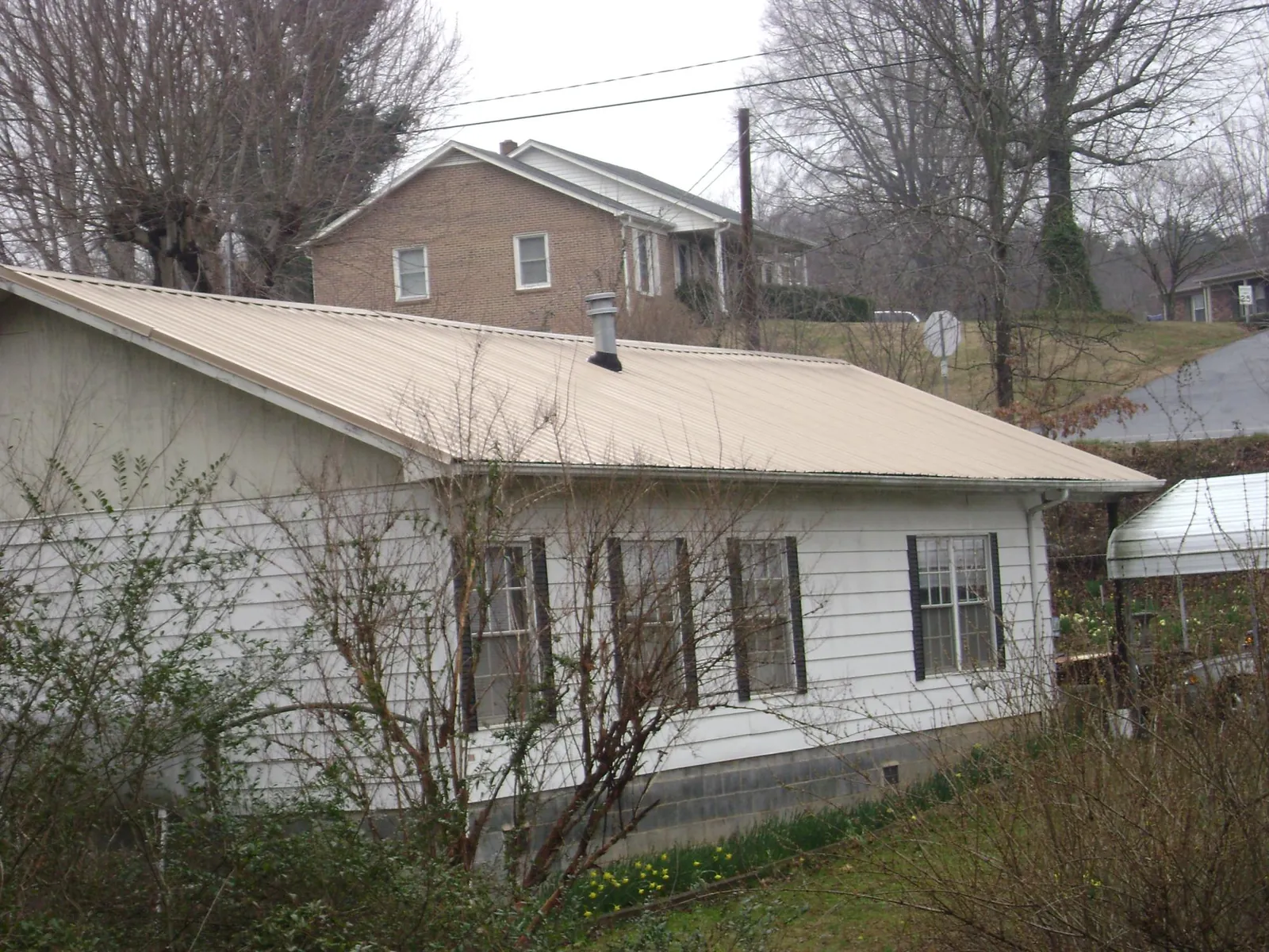 Tan metal roof on a white sided house set into a hillside — Commercial Roofing by Roofing Brothers in East New Market